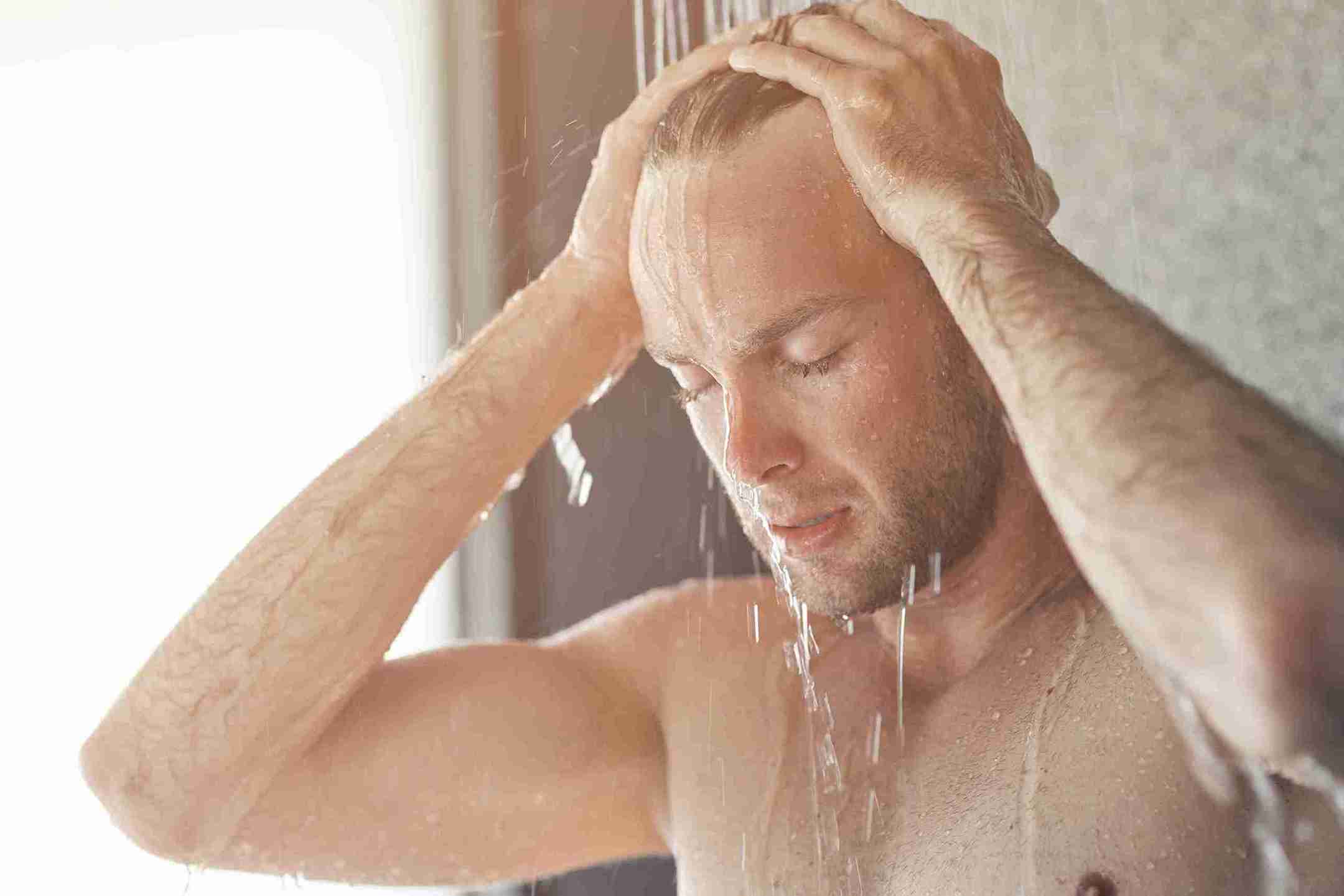 Man showering with water running over his head, illustrating the topic Does Hard Water Cause Hair Loss and its effects on hair health.